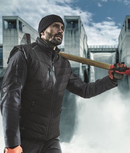 Man in black work clothes with an axe in front of a water dam.
